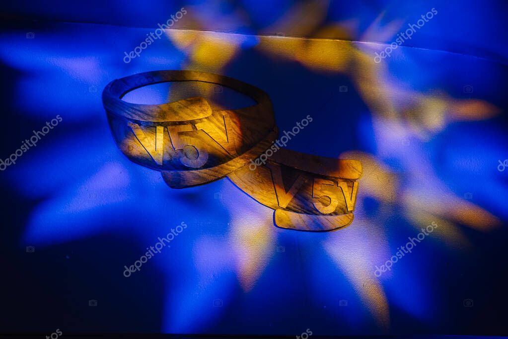 Valmiera, Latvia - March 7, 2025 - Decorative wooden V5V emblem mounted on a wall, illuminated with colorful blue and yellow stage lighting, likely part of an event or ceremony decor