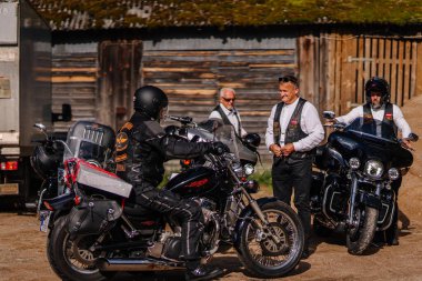 Valmiera, Letonya - 20 Haziran 2025: Motosikletli bir grup motosikletli, deri ceketli adamlar hikayelerini paylaşıyor ve güneşli havanın tadını çıkarıyorlar