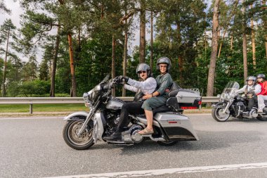 Valmiera, Letonya - 20 Haziran 2025: İki kadın bisikletçi, arka planda ağaçlar ve yemyeşil yeşilliklerle dolu güzel bir yolda motosiklet sürmenin tadını çıkarıyorlar