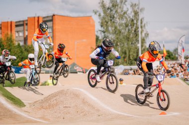 Valmiera, Letonya - 12 Temmuz 2025: BMX Avrupa Şampiyonası. Canlı formalarla BMX yarışçıları toprak pistte tezahürat yapan kalabalığın arkasında yarışıyorlar.