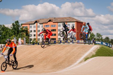 Valmiera, Letonya - 12 Temmuz 2025: BMX Avrupa Şampiyonası. BMX sürücülerinden oluşan bir grup geride binalarla toprak yolda sıçrayışlar yapıyor.