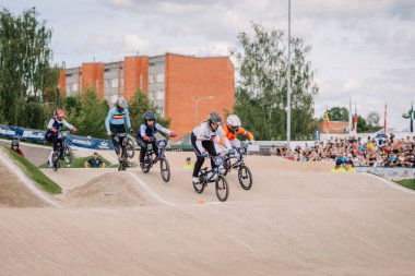 Valmiera, Letonya - 12 Temmuz 2025: BMX Avrupa Şampiyonası. BMX yarışçıları arka planda izleyicilerle toprak pistte geziniyorlar ve etkinliğin tadını çıkarıyorlar