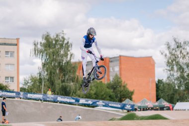 Valmiera, Letonya - 12 Temmuz 2025: BMX atleti şehir manzarası ve seyircileriyle bir kaykay parkında havada süzülüyor. BMX Avrupa Şampiyonası