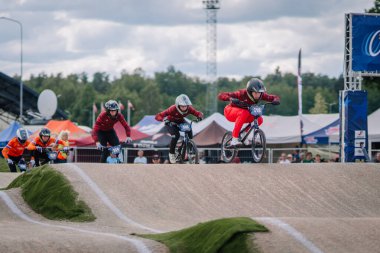 Valmiera, Letonya - 12 Temmuz 2025: BMX yarışçıları arka planda renkli çadırlar ve coşkulu izleyicilerle pistte yarışıyorlar. BMX Avrupa Şampiyonası