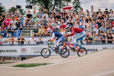 Valmiera, Letonya - 12 Temmuz 2025: Arkalarında tezahürat yapan bir kalabalık ile iki BMX yarışçısı Letonya şampiyonasında yoğun bir şekilde yarışıyor. BMX Avrupa Şampiyonası