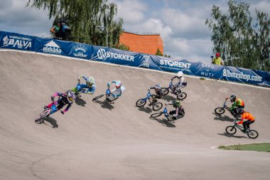 Valmiera, Letonya - 12 Temmuz 2025: BMX yarışçıları, heyecan verici açık hava olayının keyfini çıkaran seyircilerle yoğun bir şekilde kavisli bir pistte yarışıyorlar. BMX Avrupa Şampiyonası