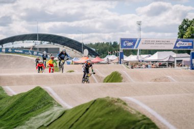 Valmiera, Letonya - 12 Temmuz 2025: BMX yarışçıları Avrupa Şampiyonası 'nda bir açık pistte canlı yeşil tepelerle yarışıyorlar