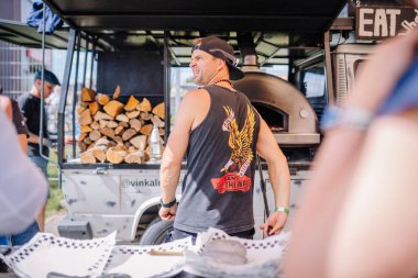 Valmiera, Letonya - 12 Temmuz 2025: Erkek aşçı arka planda odun yığını olan bir açık hava yemek kamyonunda lezzetli yemekler hazırlıyor. BMX Avrupa Şampiyonası.