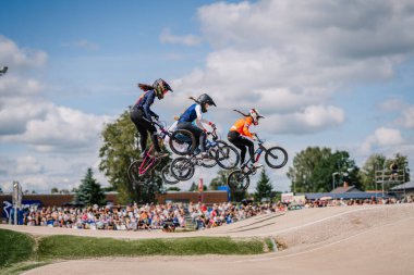 Valmiera, Letonya - 12 Temmuz 2025: Heyecan verici bir bisiklet yarışması sırasında BMX motosikletli üç kadın havada süzülüyor. BMX Avrupa Şampiyonası