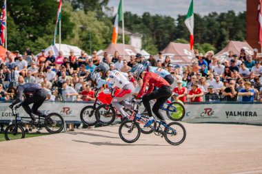Valmiera, Letonya - 12 Temmuz 2025: BMX Avrupa Şampiyonası. BMX sürücüleri toprak pistte tezahürat yapan kalabalık ve bayraklarla yarışıyorlar.