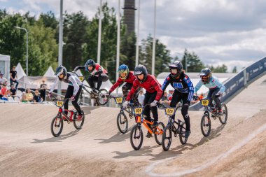 Valmiera, Letonya - 12 Temmuz 2025: BMX Avrupa Şampiyonası. Genç erkek BMX sürücüleri toprak pistte arka planda seyircilerle yarışıyor