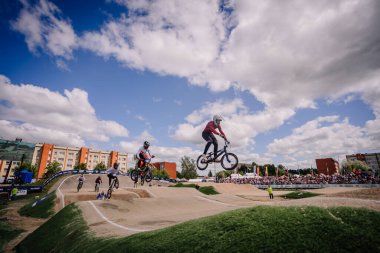 Valmiera, Letonya - 12 Temmuz 2025: BMX Avrupa Şampiyonası. Rekabetçi BMX sürücüleri yakınlardaki kalabalıkla toprak pistte sıçrama yapıyorlar.