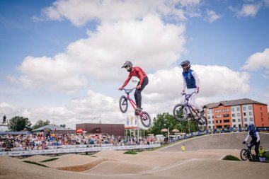 Valmiera, Letonya - 12 Temmuz 2025: BMX Avrupa Şampiyonası. Erkek BMX sürücüleri heyecan verici bir yarışta havada süzülüyor. Seyirciler izliyor.