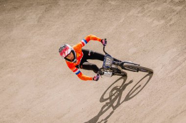 Valmiera, Letonya - 12 Temmuz 2025: BMX Avrupa Şampiyonası. Turuncu formalı kadın BMX bisikletçi toprak pistte yarışıyor, yetenek ve hız gösteriyor.