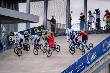 Valmiera, Letonya - 12 Temmuz 2025: BMX Avrupa Şampiyonası. Canlı giysiler içinde BMX yarışçıları bisiklet yarışının başlangıcından başlayarak arkalarında kalabalıkla