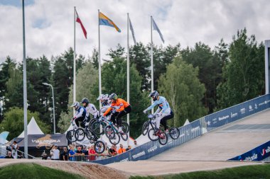 Valmiera, Letonya - 12 Temmuz 2025: BMX Avrupa Şampiyonası. BMX sürücülerinden oluşan bir grup, yakınlarda bayraklar ve izleyicilerle pistte sıçrama yapıyor.
