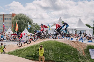 Valmiera, Letonya - 12 Temmuz 2025: BMX Avrupa Şampiyonası. Heyecan verici BMX yarışı. Toprak pistte birden fazla yarışçı ve tezahürat yapan kalabalık var.