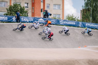 Valmiera, Letonya - 12 Temmuz 2025: BMX Avrupa Şampiyonası. BMX yarışçıları, arka planda izleyiciler ve canlı afişler bulunan bir pistte yol alıyorlar.