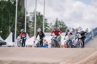 Valmiera, Letonya - 12 Temmuz 2025: BMX Avrupa Şampiyonası. Bir grup BMX yarışçısı heyecan verici yarışı izleyen izleyicilerle toprak yolda hız yapıyor.