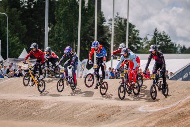 Valmiera, Letonya - 12 Temmuz 2025: BMX Avrupa Şampiyonası. Renkli BMX yarışçıları arka planda coşkulu izleyicilerle toprak pistte yarışıyor