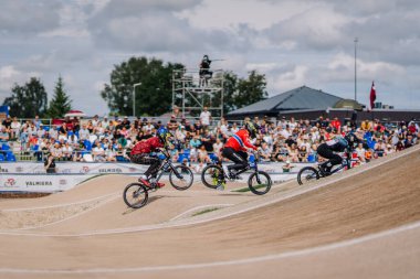 Valmiera, Letonya - 12 Temmuz 2025: BMX Avrupa Şampiyonası. BMX yarışçıları toprak yolda, yakınlarda coşkulu izleyiciler var.