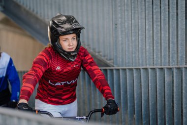 Valmiera, Letonya - 12 Temmuz 2025: BMX Avrupa Şampiyonası. Kırmızı formalı kadın BMX sürücüsü engelli kentsel bisiklet pistinde yarıştan önce odaklandı