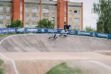 Valmiera, Letonya - 12 Temmuz 2025: BMX Avrupa Şampiyonası. BMX binicileri canlı bayraklar ve binalarla çevrili kavisli bir pistte yarışıyorlar.