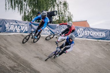 Valmiera, Letonya - 12 Temmuz 2025: BMX Avrupa Şampiyonası. BMX yarışçıları, Stokker markalaşması ve dinamik enerji içeren toprak yolda hareket halindeler