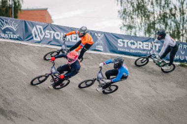 Valmiera, Letonya - 12 Temmuz 2025: BMX Avrupa Şampiyonası. BMX yarışçıları renkli pankartlarla toprak pistte yarışarak enerjik bir atmosfer yaratıyorlar.
