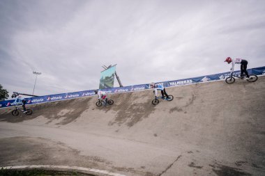 Valmiera, Letonya - 12 Temmuz 2025: BMX Avrupa Şampiyonası. BMX sürücüleri bulutlu gökyüzünün altındaki bir spor etkinliği sırasında eğri bir pistte yeteneklerini sergiliyorlar.