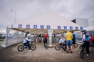 Valmiera, Letonya - 12 Temmuz 2025: BMX Avrupa Şampiyonası. Genç bisikletçiler büyük bir çadırın altında numaralandırılmış bölümlerle bir yarışa hazırlanıyorlar.