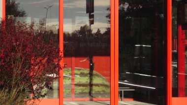 Valmiera, Letonya - 17 Ekim 2025: Çeşitli insanlar cam kapılı parlak turuncu bir binaya yaklaşıp içeri giriyor, kamera hareketlerini takip ediyor