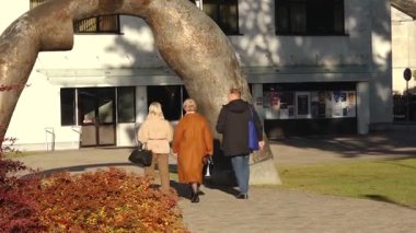 Valmiera, Letonya - 17 Ekim 2025: Arkadaşlar çarpıcı bir heykelin altındaki parkta geziniyor, kamera onları takip ediyor ve sahneyi kaydediyor.