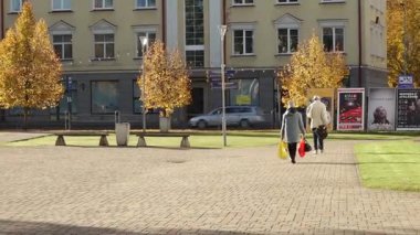 Valmiera, Letonya - 17 Ekim 2025: İki kişi hareketli bir sonbahar parkında geziniyor, kamera onları renkli ağaçlar ve kentsel zemin gösteren bir hareketle takip ediyor