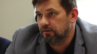 Valmiera, Letonya - 17 Ekim 2025: Spor ceketli sakallı bir adam toplantı sırasında görüşlerini paylaşıyor, kamera ifadelerini ve nişanlarını kaydediyor