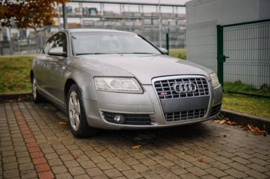 Valmiera, Letonya - 23 Ekim 2025: Gümüş renkli Audi S6 yeşil çimenler ve endüstriyel yapılarla çevrili bir kaldırım taşına park edilmiştir.