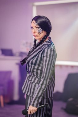 Benzersiz yüz boyası ve örgülü saç stili olan, şık çizgili takım elbiseli, sahnede duran, kendine güveni ve sanatsal yeteneği olan bir sanatçı.