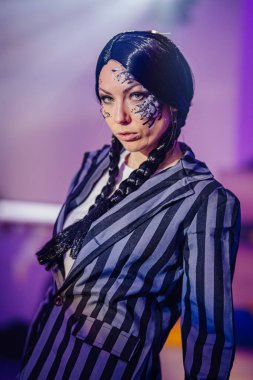 Örgülü saçlı, çarpıcı makyajlı, çizgili takım elbiseli, renkli pozlar veren, cesur moda tercihleri ve yaratıcı sanatlar yapan bir model.