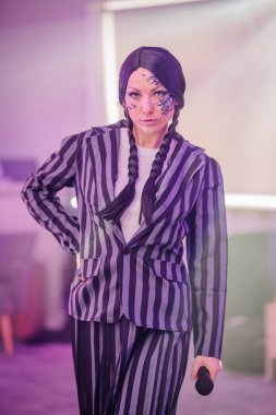 Kendine güvenen makyajlı, örgülü saç stili, kalın çizgili takım elbiseli, sahnede mikrofon tutan, sanatsal enerji saçan kendine güvenen bir kadın sanatçı.