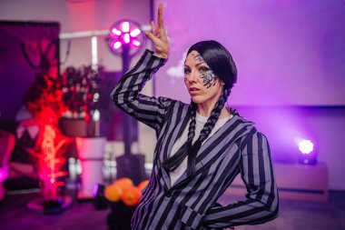 Çarpıcı yüz boyası ve örgülü saç stiliyle renkli ışıklar ve sanatsal bir atmosferle çevrili çizgili bir kıyafetle yaratıcı enerjiyi yakalayan sanatçı.