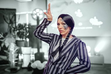 Çarpıcı yüz sanatına sahip model, canlı bir arkaplan arasında cesur moda tercihleri ve sanatsal yetenekleri vurguluyor.