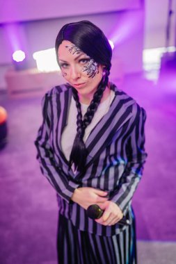 Kendine güvenen, örgülü saçlı, eşsiz yüz boyalı, çizgili takım elbiseli, renkli ışıklandırmalı, sanatsal yetenekleri olan bir kadın sanatçı.