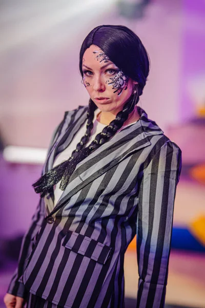 Çizgili takım elbiseli kendinden emin bir kadın model, çarpıcı bir yüz makyajı içeriyor, renkli bir ortamda poz veriyor, moda ve yaratıcılığı ön plana çıkarıyor.