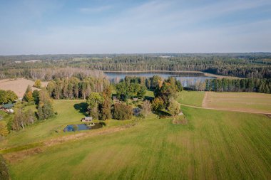 Canlı yeşil alanlar, sakin bir gölet ve çevreleyen ağaçlarla dolu, kırsal yaşamın sükunetini gösteren huzurlu bir kırsal alan manzarası.