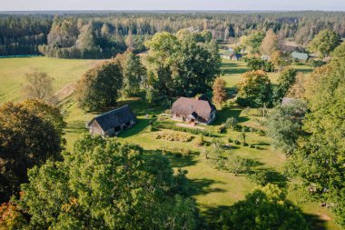 Canlı ağaç ve tarlaların arasına yerleşmiş, kırsal hayatın sükunetini ve doğal güzelliğini vurgulayan kırsal bir evin manzaralı havası.