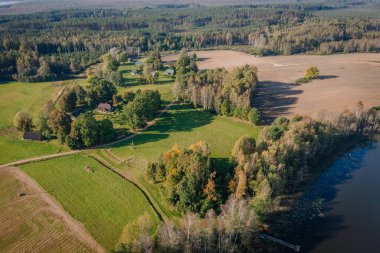 Sakin bir nehrin yanında canlı tarlaların ve çeşitli ağaçların manzaralı perspektifi kırsal alanların ve doğal çevrenin dingin güzelliğini vurguluyor.