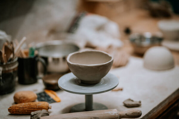 Pottery wheel with an unfinished ceramic bowl, surrounded by various tools and materials, highlighting the creative process in a warm workshop atmosphere