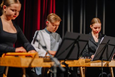 Valmiera, Letonya - 08 Mayıs 2025: Sahnede geleneksel enstrümanlar çalan üç genç müzisyen, canlı bir konser atmosferinde müzik konusundaki becerilerini ve tutkularını vurguluyor