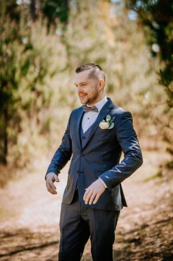 Sofistike bir takım elbise giymiş ağaçlar ve doğa ile çevrili canlı bir ortamda gülümseyen bir adam kutlama anında neşe ve zarafeti somutlaştırıyor.