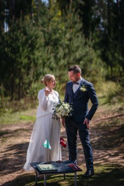 Düğün kıyafetli bir çift, yeşil ile çevrili, sakin bir açık havada duruyor, hassas bir anı paylaşıyor, sevgi ve kutlama sergiliyor.